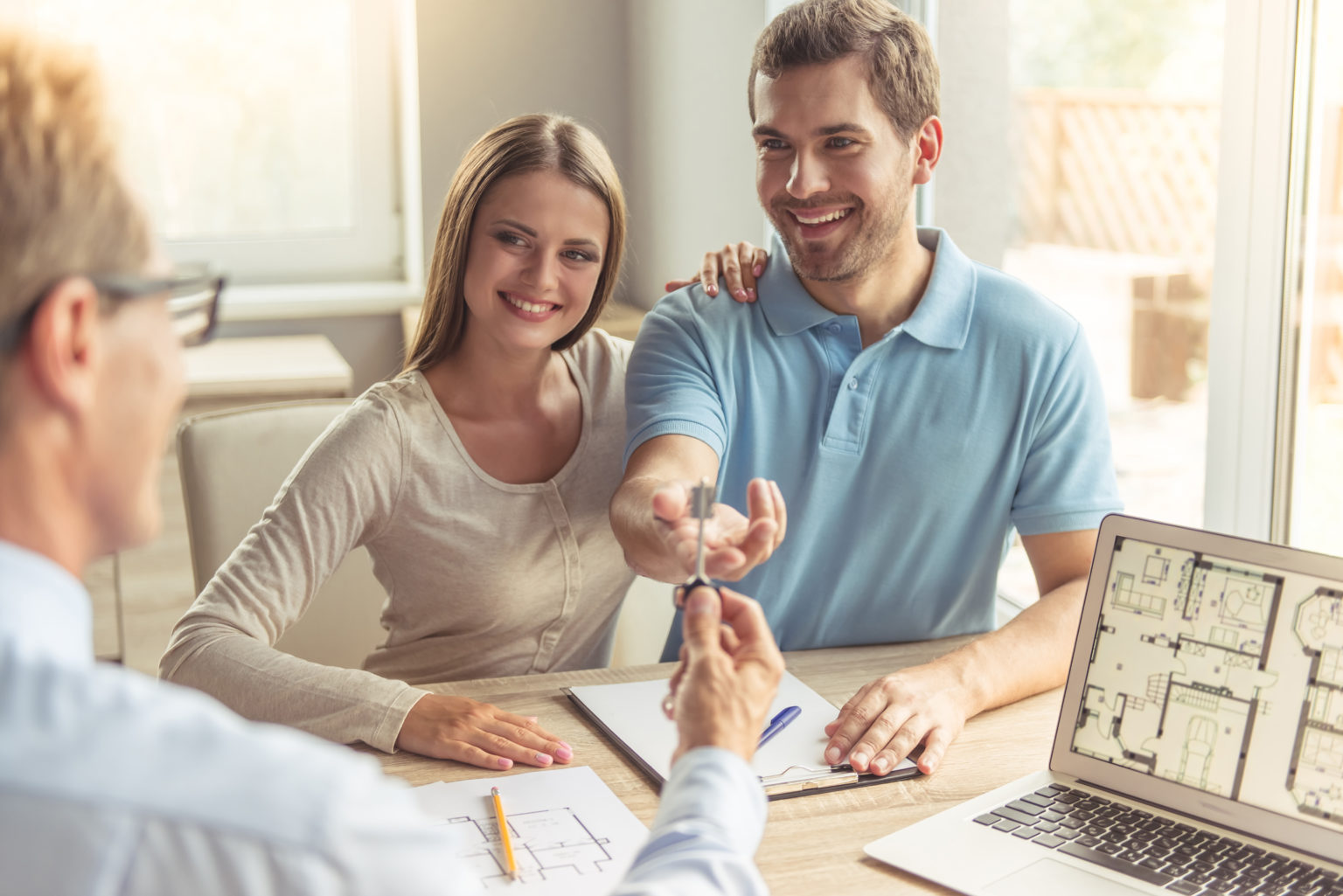 Handsome realtor in classic shirt is giving key of the new apartment to happy young couple while they are sitting in the office